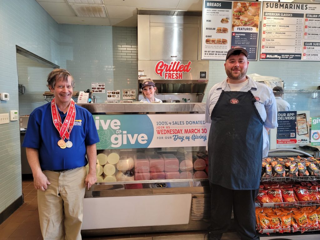 Jersey Mikes - Employee and SONorCal in front of "Day of Giving" signage