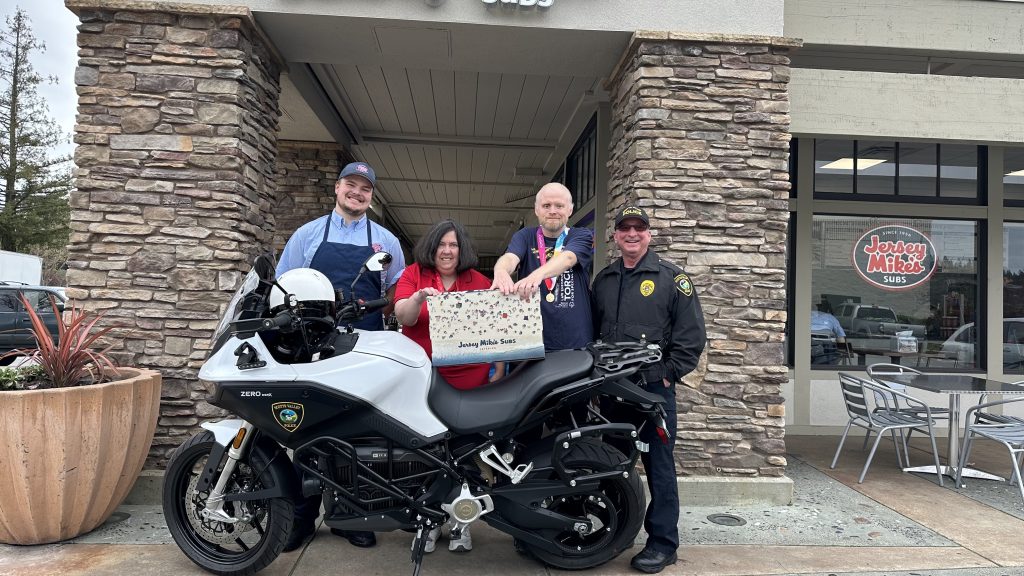 Jersey Mikes - Jersey Mike's employee, athletes, and police officer in front of storefront