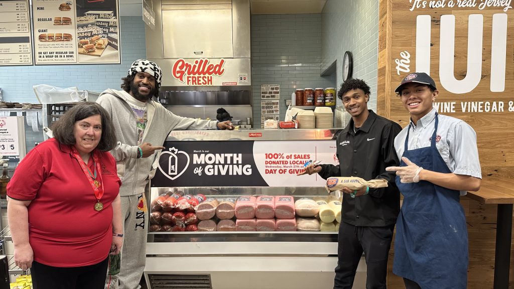 Jersey Mikes - Santa Clara University and athlete pointing to "Month of Giving" signage