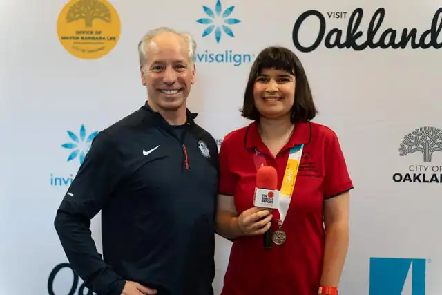 Blog - Alysa Liu - Sophia with Alysa's coach Phil DiGuglielmo at the Invisalign/Visit Oakland
backdrop.